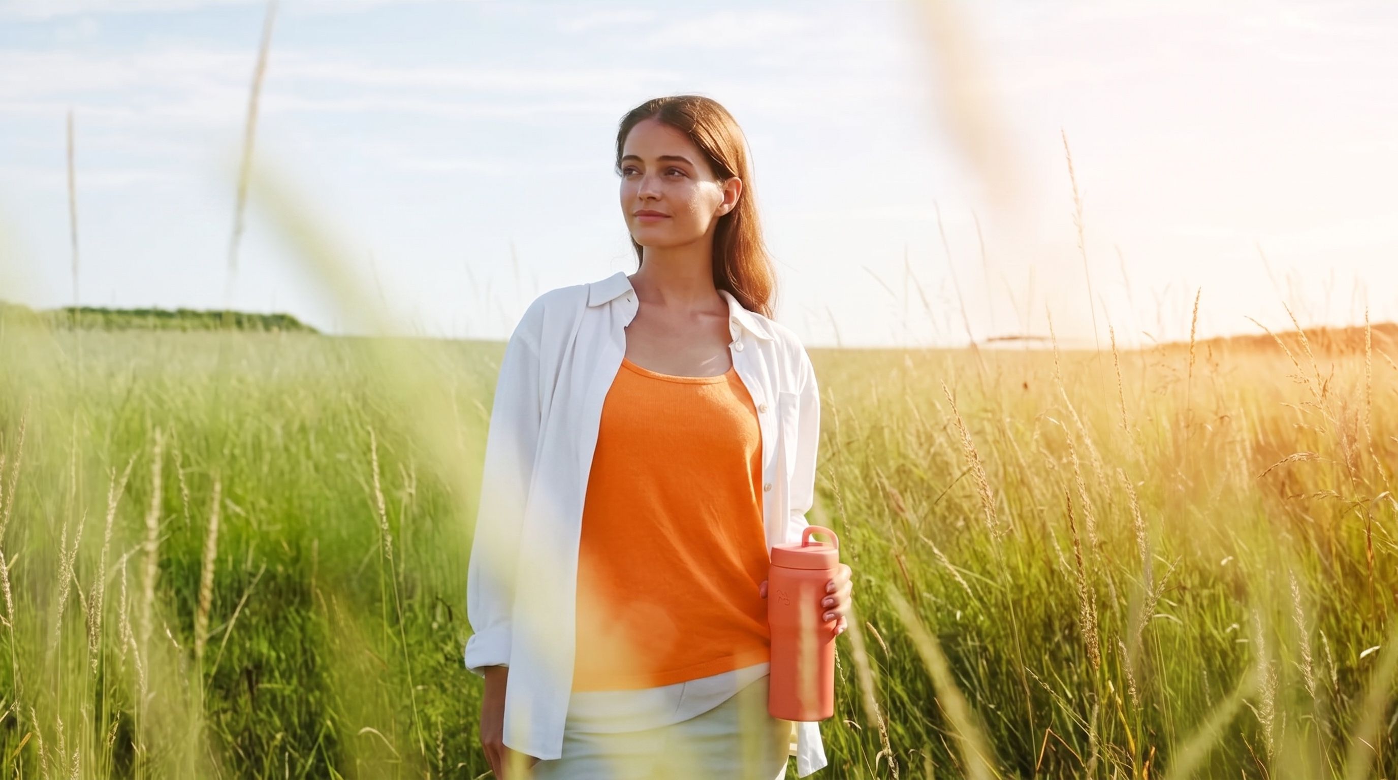 A woman standing in a golden meadow at sunset, looking ahead calmly
