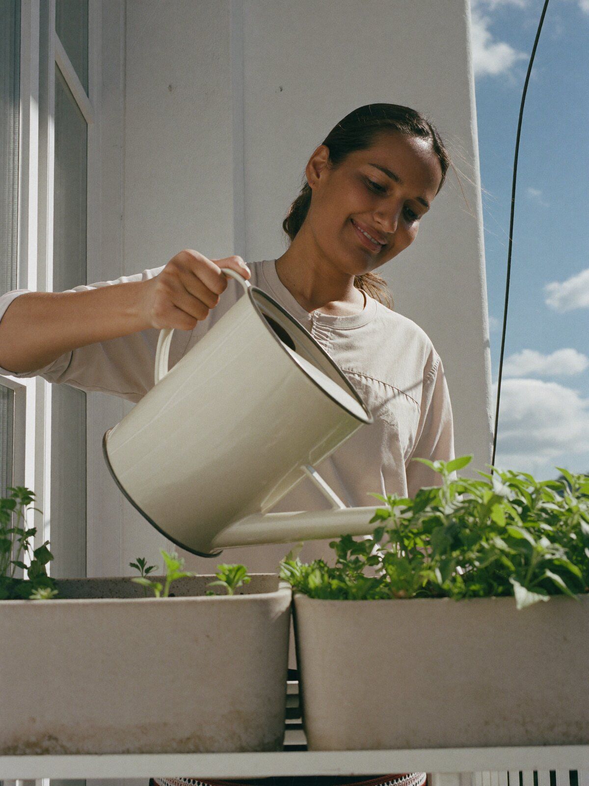 A woman watering herbs on a small balcony